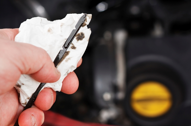 person holding dipstick and cloth with motor oil present