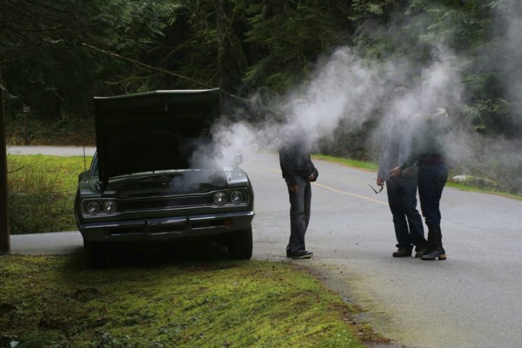 three people on the side of the road with smoke emitting from the hood of a car