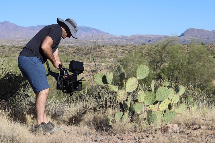 person holding video camera next to prickly pear cacti