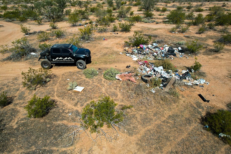 black pickup truck facing large pile of trash in desert