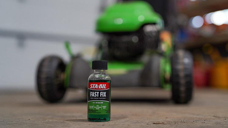 bottle of STA-BIL Fast Fix sitting on the floor of garage with lawn mower in background out of focus