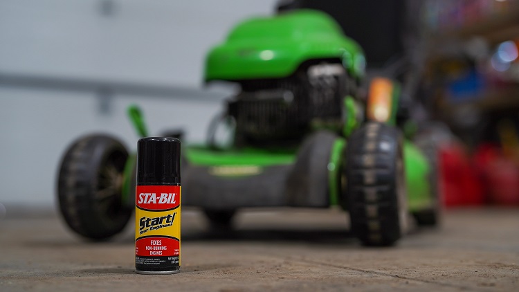 bottle of STA-BIL Start Your Engines sitting on floor of garage in front of lawn mower