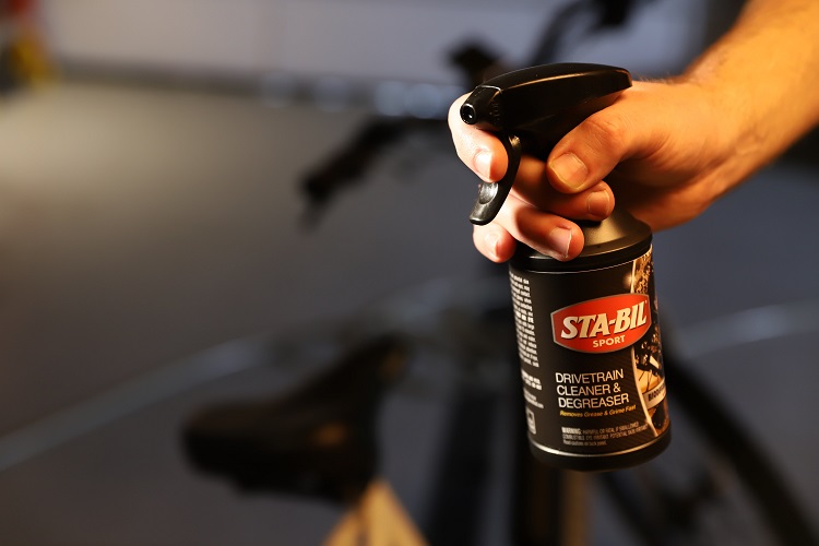 person holding bottle of STA-BIL SPORT Bike Drivetrain Cleaner & Degreaser with bike in background
