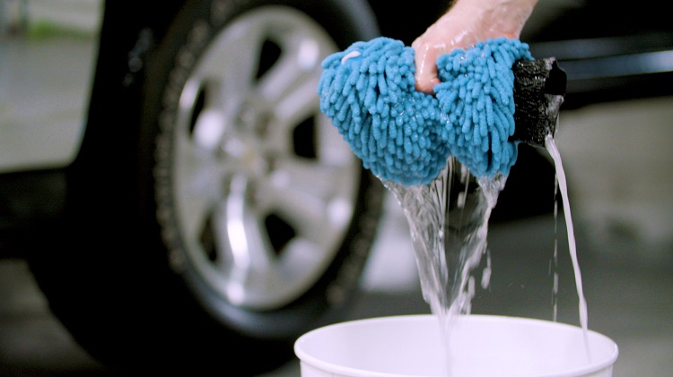 hand squeezing wash mitt as water pours into bucket