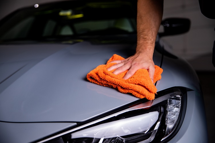 person using microfiber towel on hood of luxury sedan