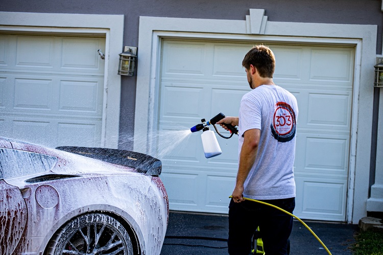 person using pressure washer and 303 Foam Cannon to wash a sports car