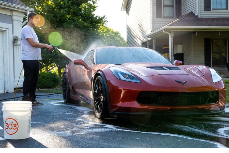 person using pressure washer to rinse away soap suds from a sports car